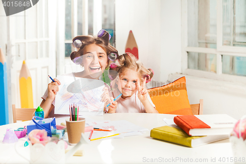 Image of The young mother and her little daughter drawing with pencils at home