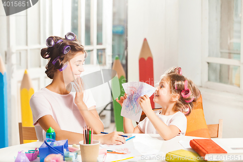 Image of The young mother and her little daughter drawing with pencils at home