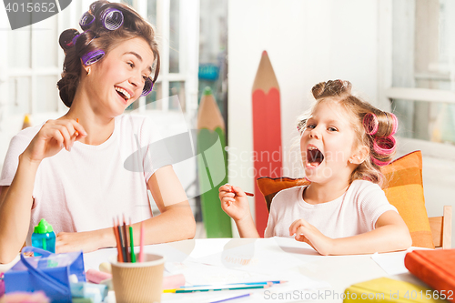 Image of The young mother and her little daughter drawing with pencils at home