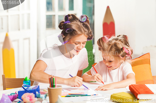 Image of The young mother and her little daughter drawing with pencils at home