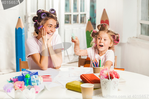 Image of The young mother and her little daughter drawing with pencils at home