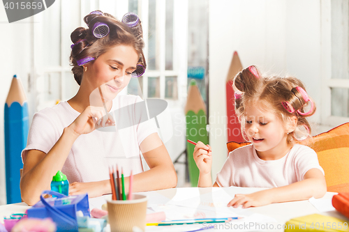 Image of The young mother and her little daughter drawing with pencils at home