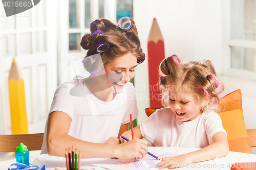 Image of The young mother and her little daughter drawing with pencils at home