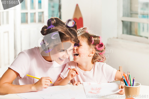 Image of The young mother and her little daughter drawing with pencils at home