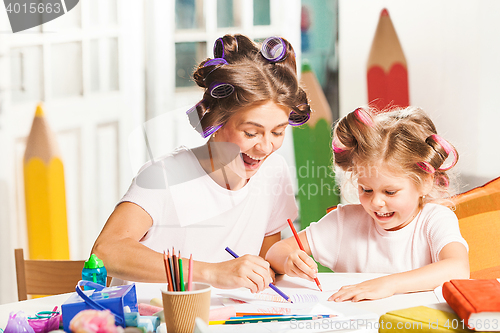 Image of The young mother and her little daughter drawing with pencils at home