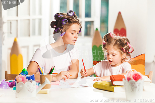 Image of The young mother and her little daughter drawing with pencils at home