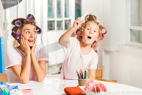 Image of The young mother and her little daughter drawing with pencils at home