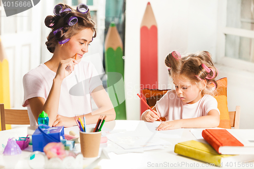 Image of The young mother and her little daughter drawing with pencils at home