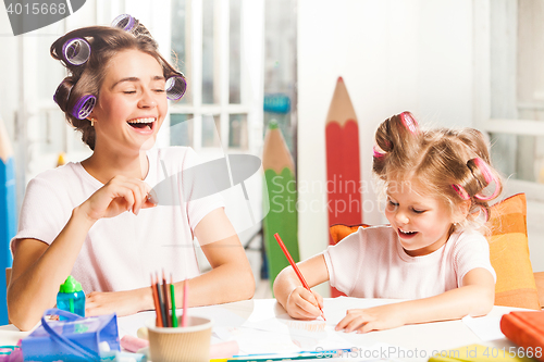 Image of The young mother and her little daughter drawing with pencils at home