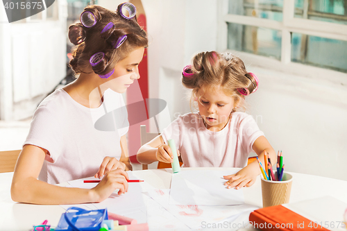 Image of The young mother and her little daughter drawing with pencils at home