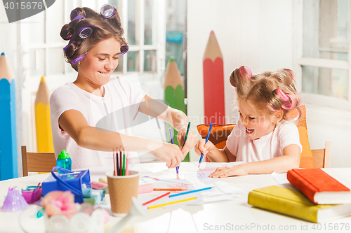 Image of The young mother and her little daughter drawing with pencils at home