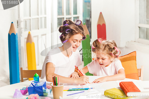 Image of The young mother and her little daughter drawing with pencils at home