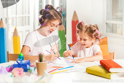 Image of The young mother and her little daughter drawing with pencils at home