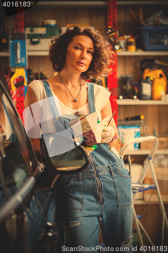 Image of adorable woman car mechanic in blue overalls with a book-instruc