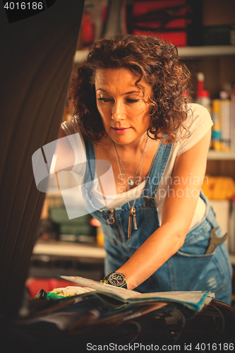 Image of mechanic woman in a blue coveralls adjusts the car\'s engine