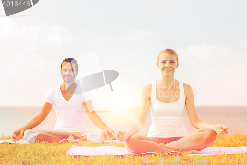 Image of smiling couple making yoga exercises outdoors