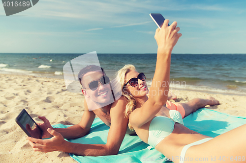 Image of happy couple with modern gadgets lying on beach