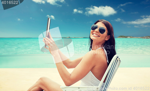 Image of smiling woman with tablet pc sunbathing on beach