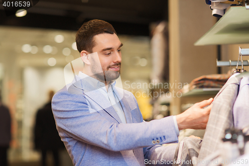 Image of happy young man choosing clothes in clothing store