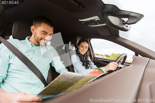 Image of happy man and woman with road map driving in car