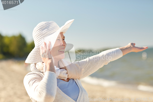 Image of happy senior woman in sun hat on summer beach