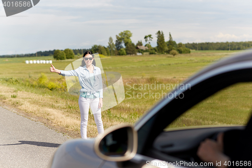 Image of woman hitchhiking and stopping car at countryside