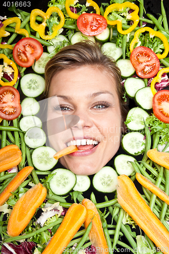 Image of Cute blond girl shot in studio with vegetables aroound the head