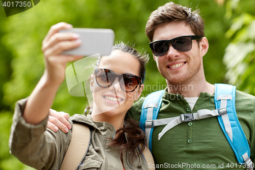 Image of couple with backpacks taking selfie by smartphone