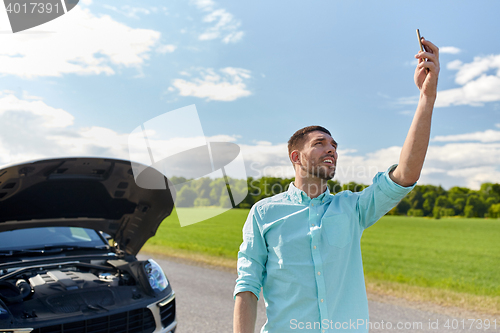 Image of man with smartphone and broken car at countryside