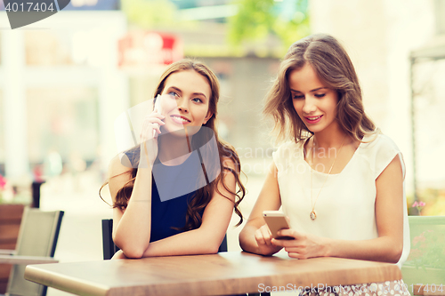 Image of happy young women with smartphones at outdoor cafe