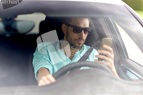 Image of man in sunglasses driving car with smartphone