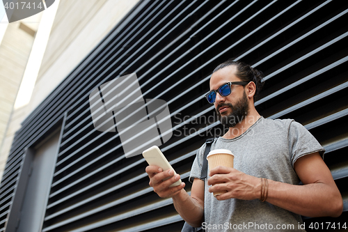 Image of man with coffee texting on smartphone in city