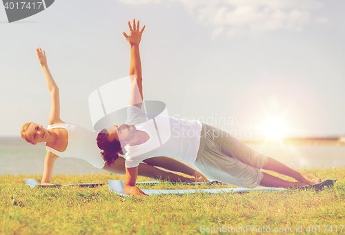 Image of smiling couple making yoga exercises outdoors