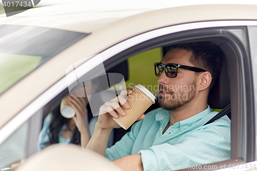 Image of happy man and woman driving in car with coffee