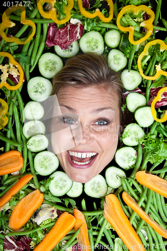 Image of Cute blond girl shot in studio with vegetables aroound the head