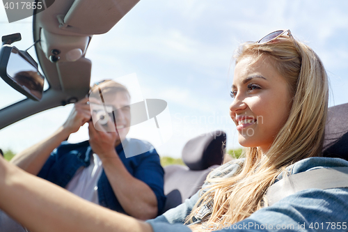 Image of happy couple with camera driving in cabriolet car