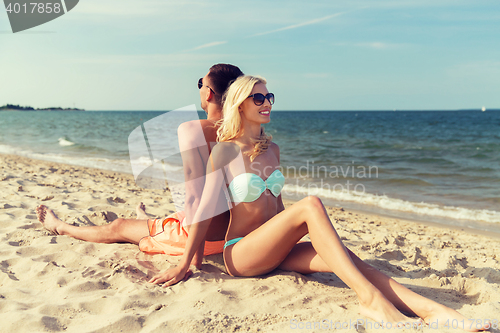 Image of happy couple in swimwear sitting on summer beach