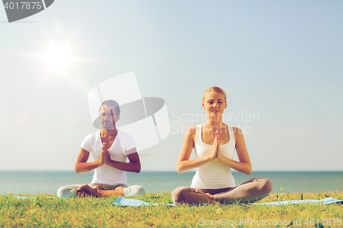 Image of smiling couple making yoga exercises outdoors