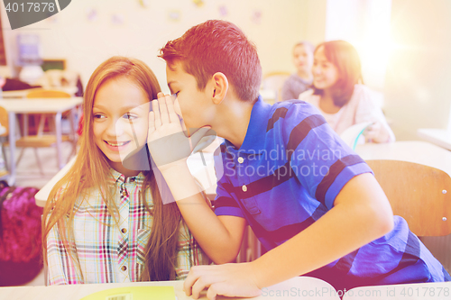 Image of smiling schoolboy whispering to classmate ear
