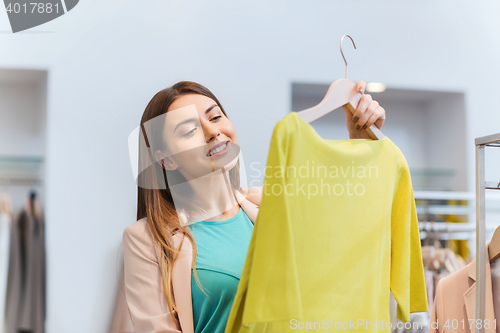 Image of happy young woman choosing clothes in mall