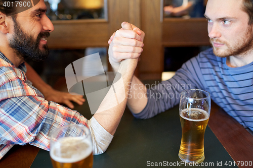 Image of happy male friends arm wrestling at bar or pub