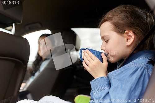 Image of little girl driving in car and drinking from cup