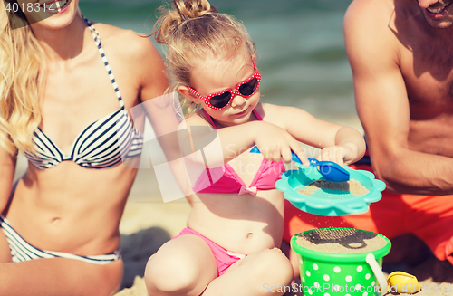 Image of happy family playing with sand toys on beach