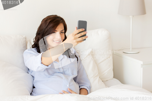 Image of pregnant woman taking smartphone selfie at home