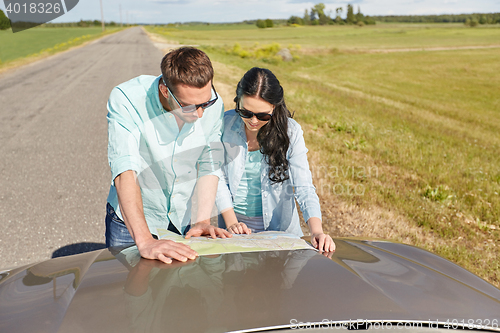 Image of happy man and woman with road map on car hood