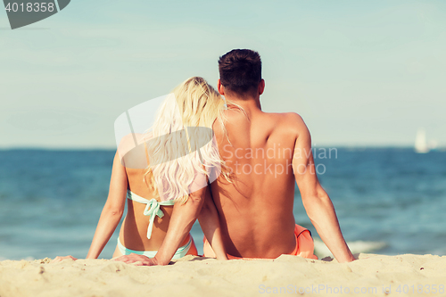 Image of happy couple in swimwear sitting on summer beach