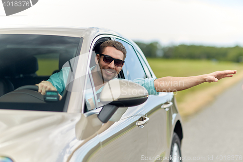 Image of happy man in shades driving car and waving hand