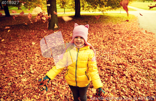 Image of happy girl playing with autumn leaves in park