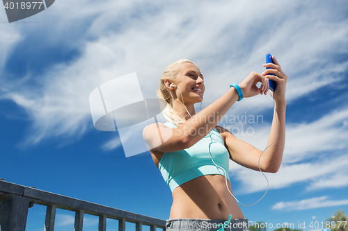 Image of happy woman with smartphone and earphones outdoors