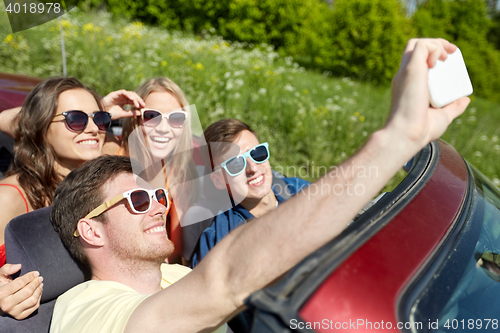 Image of friends driving in cabriolet car and taking selfie